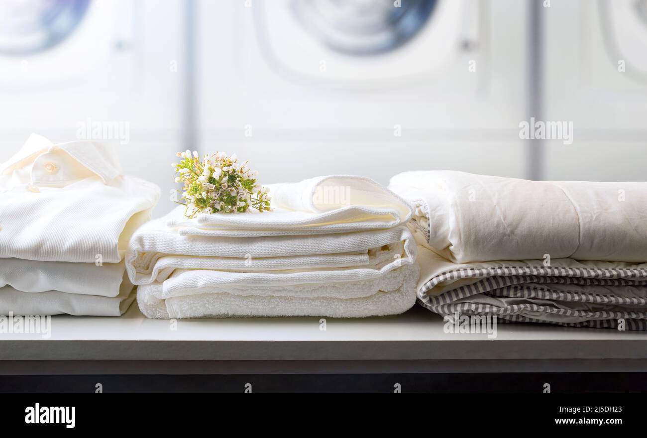 Self-service laundry for the public with bedding and staff on a white bench and professional washing machines in the background. Front view. Horizonta Stock Photo