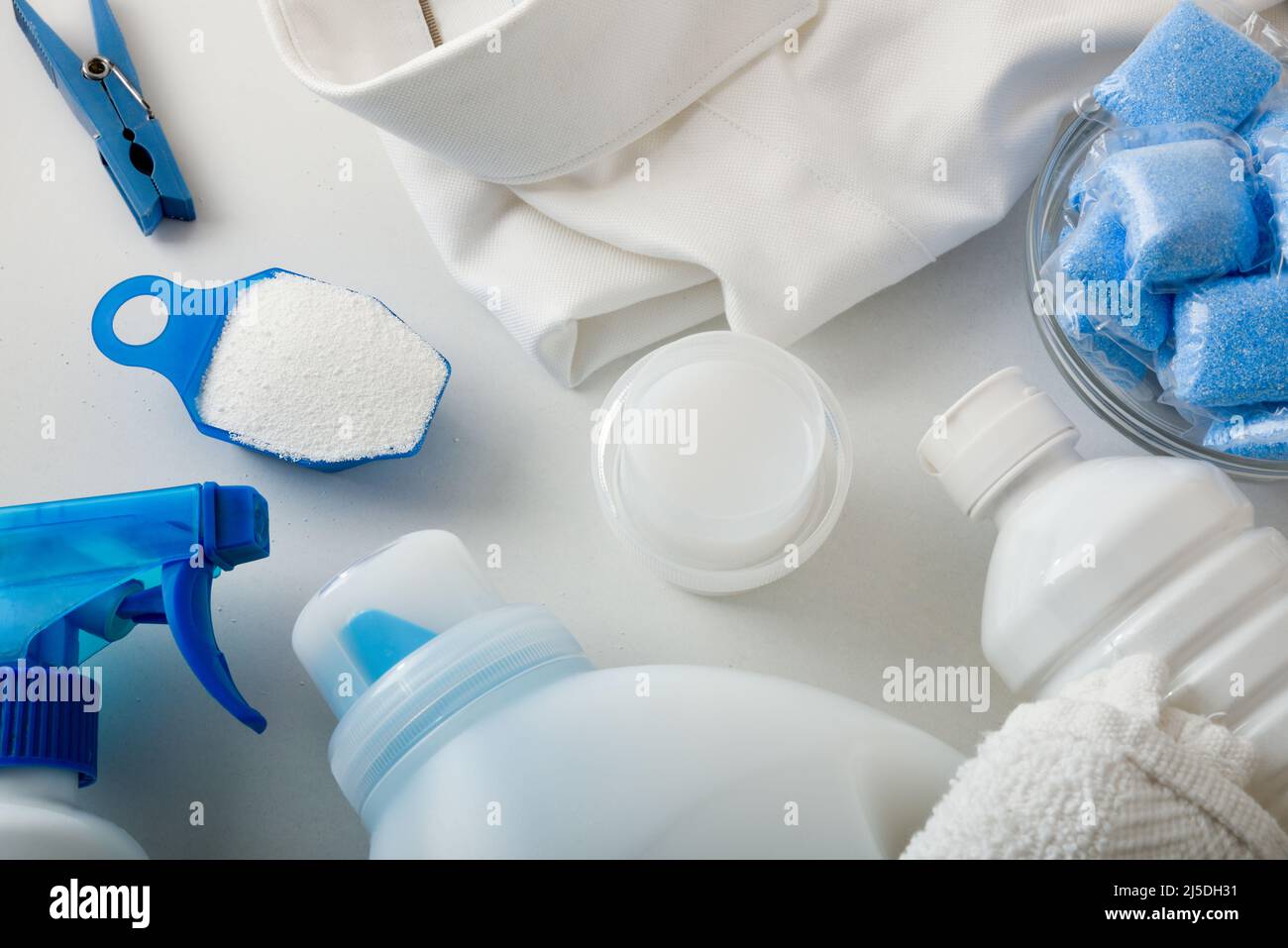 Detail of cleaning products for white clothes with shirt and towel on white table. Top view. Horizontal composition. Stock Photo