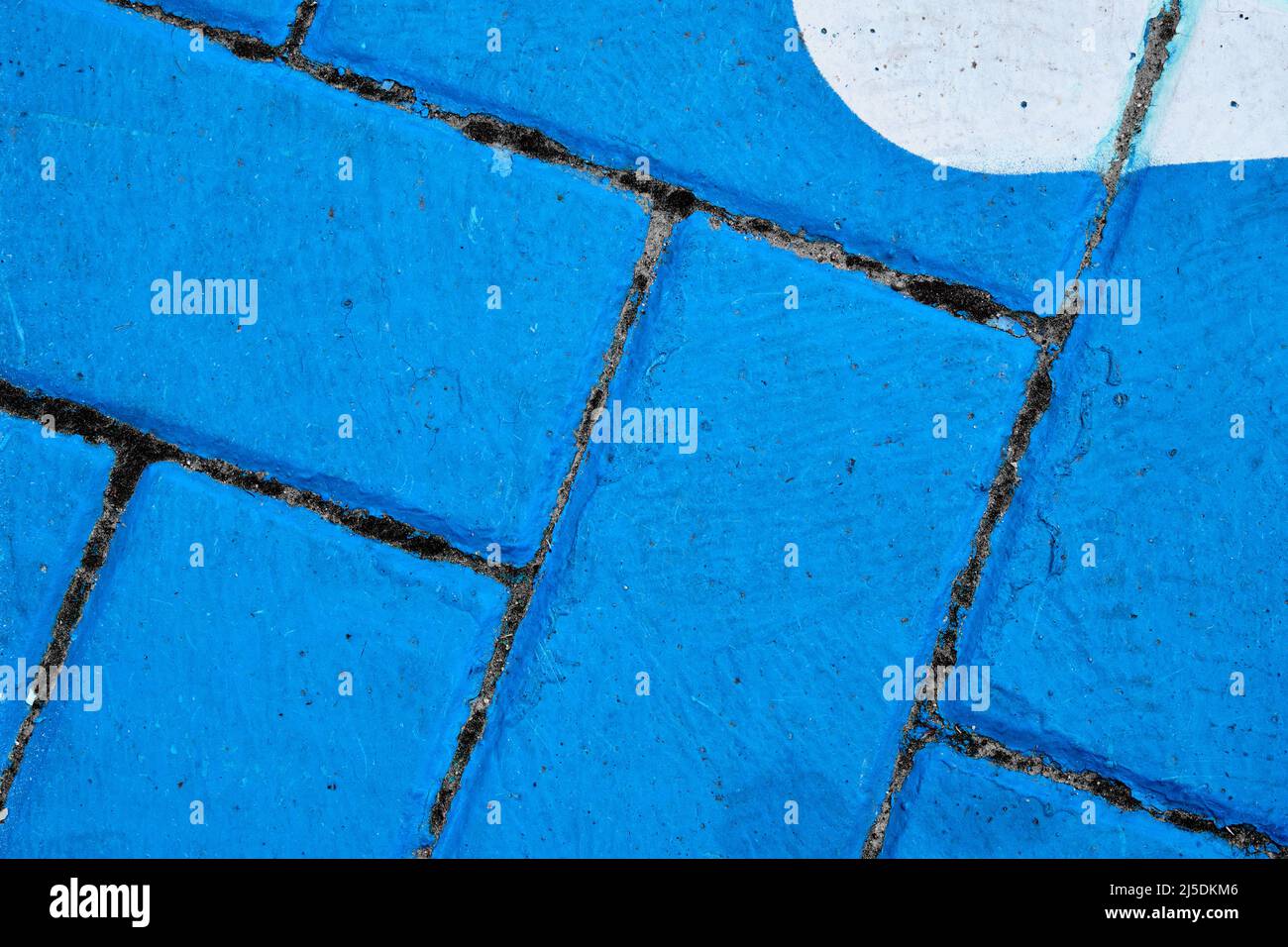 Diagonal lines of dark grout separate bricks painted blue.  An oval of white appears in the top right corner. Stock Photo