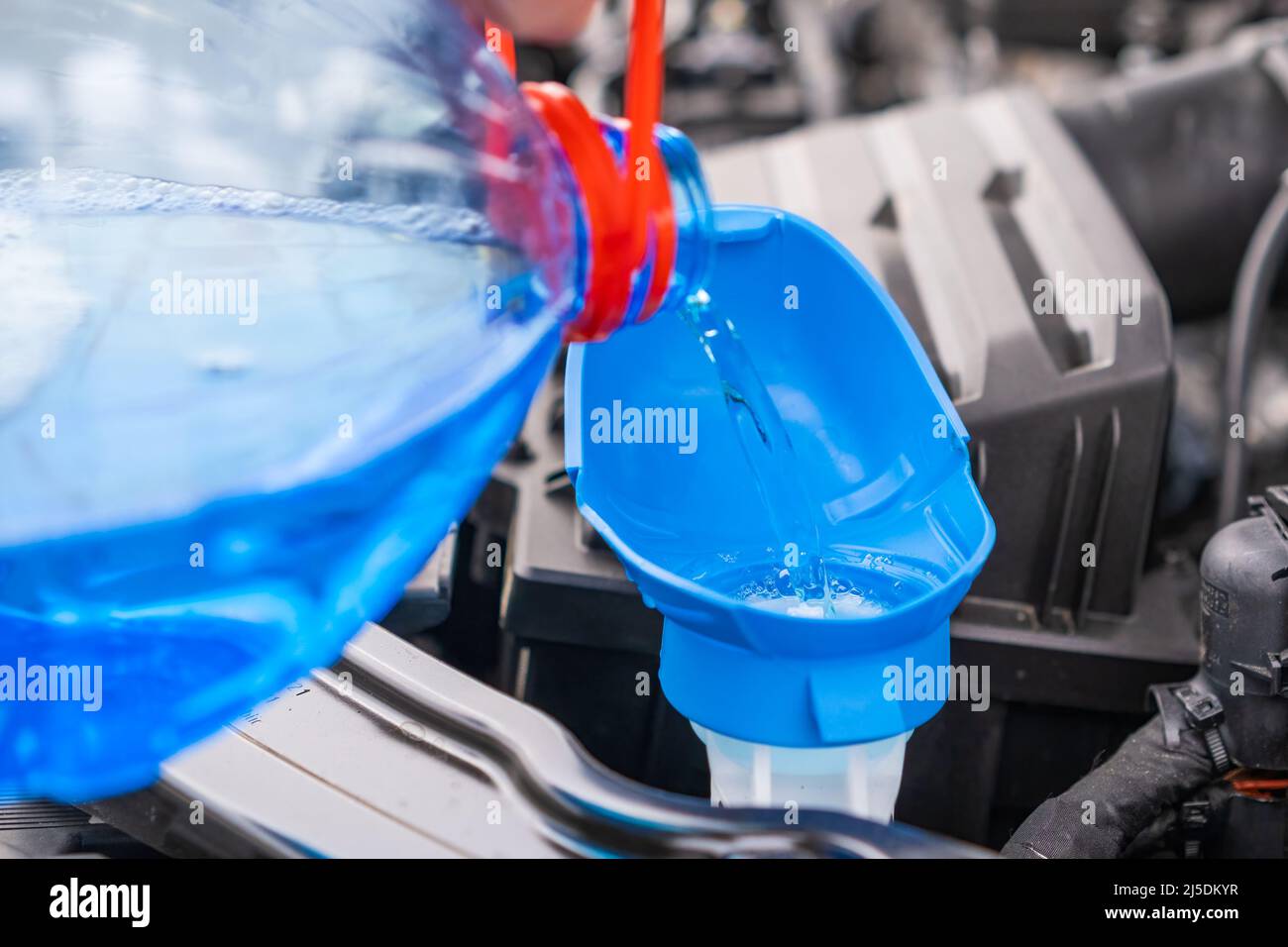 Close up driver pouring blue non freezing windshield glass washer fluid