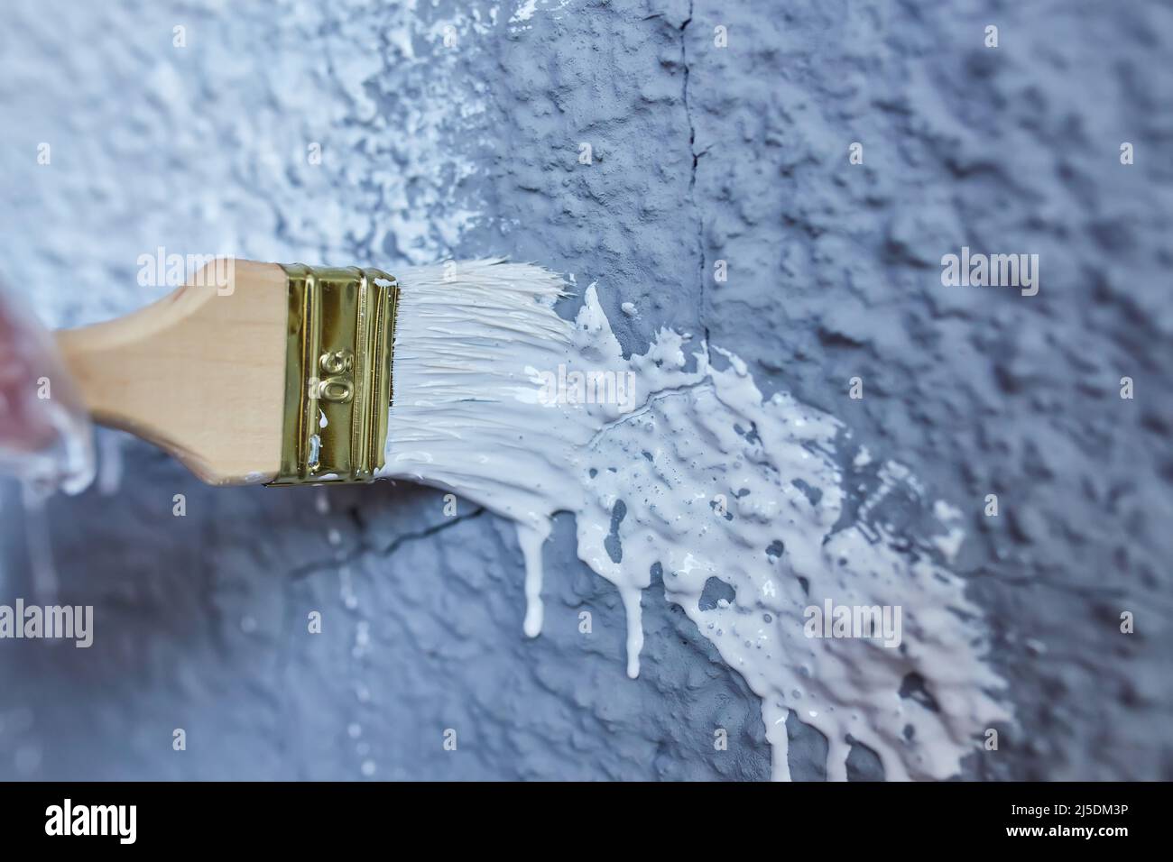 brush in hand paints the wall white paint, facade of the building Stock Photo