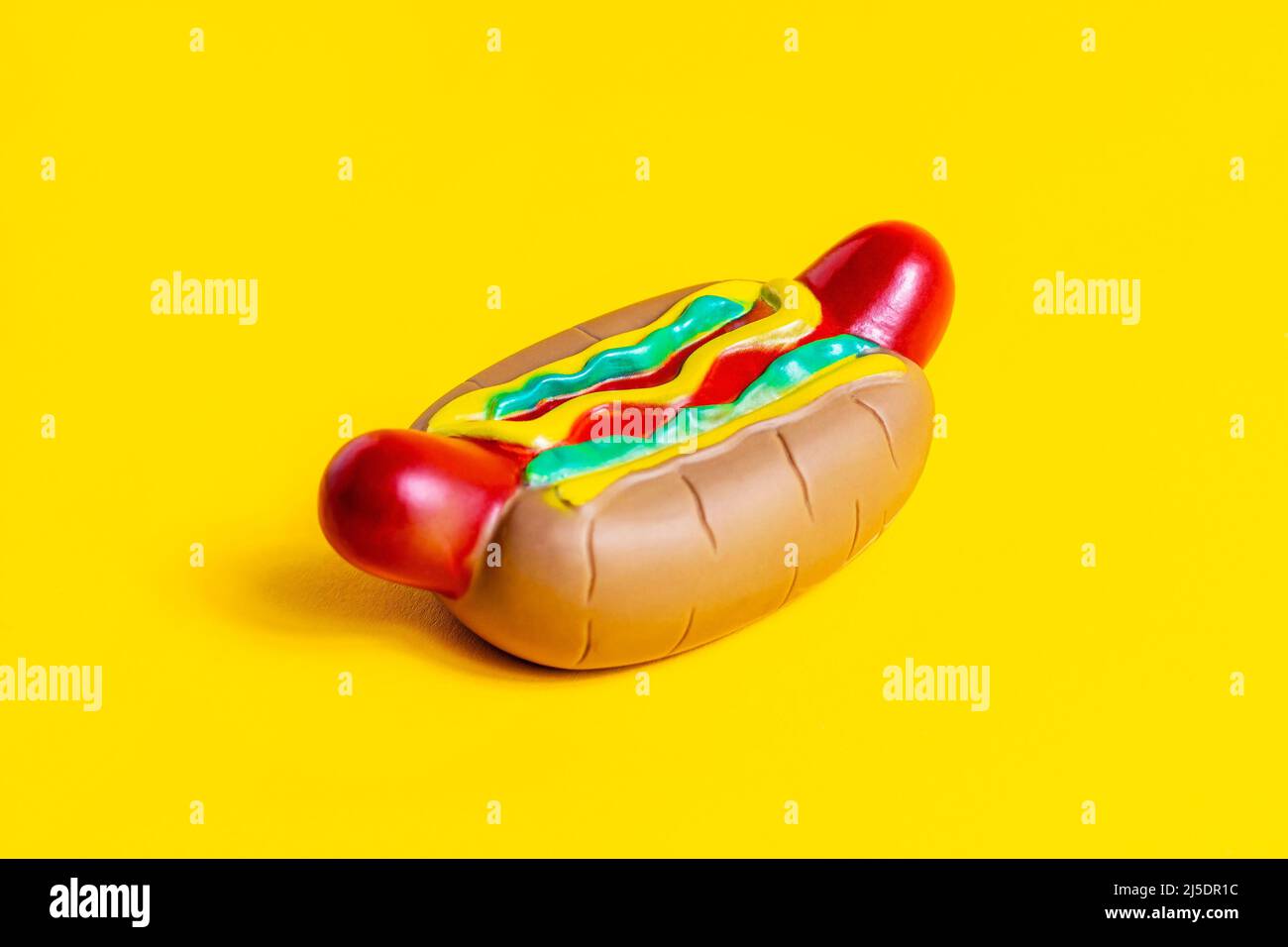 Toy American rubber hot dog with sausage, bun and mustard on bright