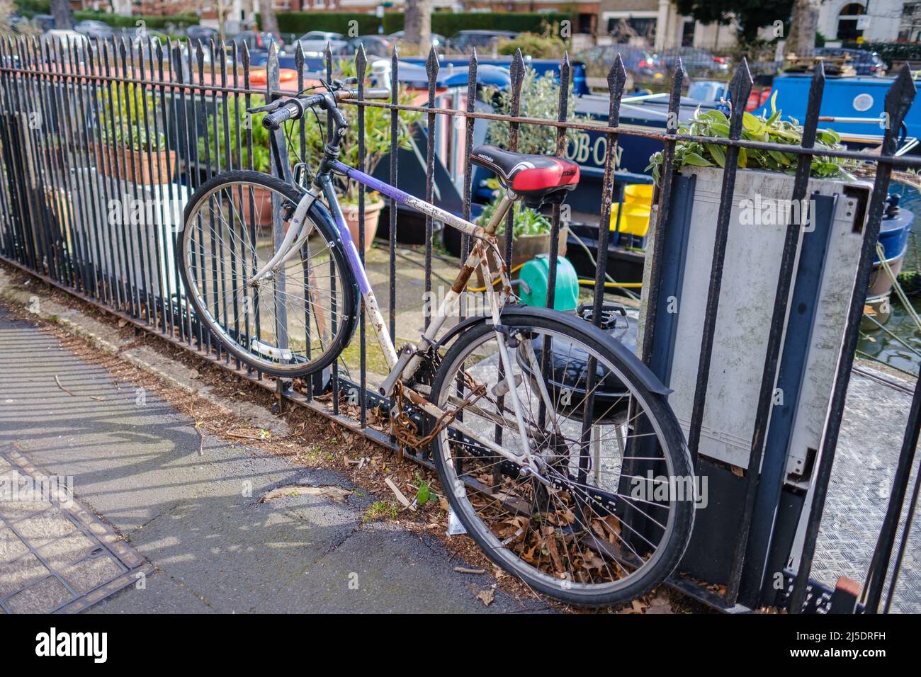 A man’s bicycle chained to the fence at Blomfield Rd. next to Regent’s Canal, Little Venice, London, England. Narrowboats & houses in background. Stock Photo
