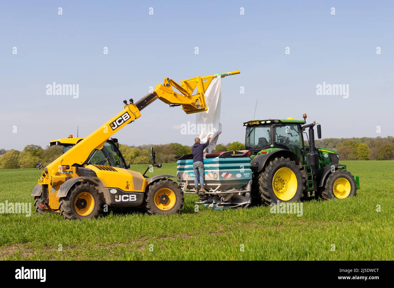 Farmworker with a telehandler loading fertiliser into a fertiliser spreader. Stock Photo