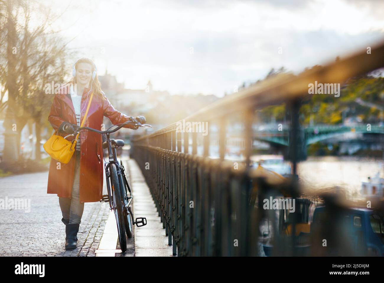 modern 40 years old woman in red rain coat with bicycle walking outside ...