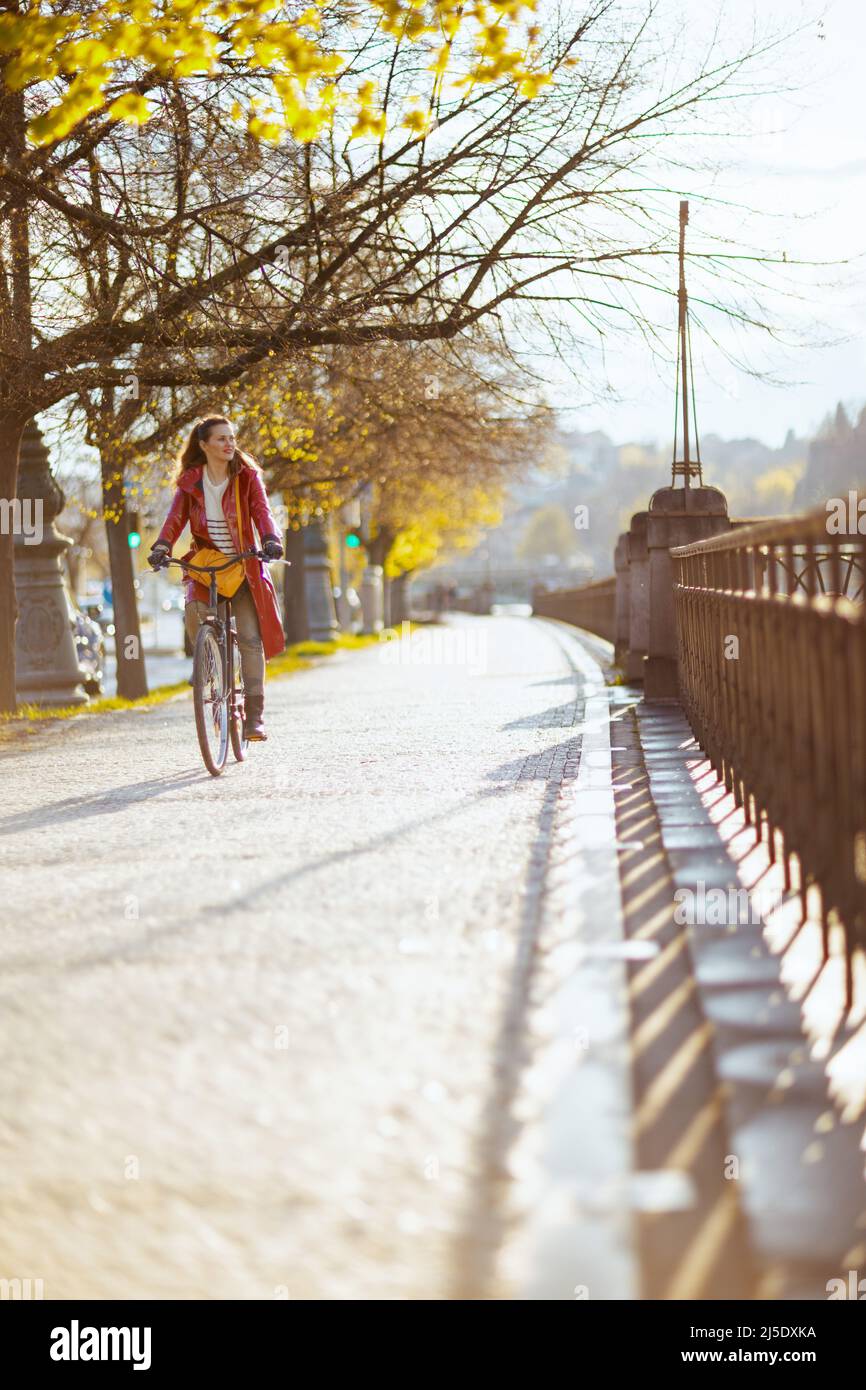 modern woman in red rain coat outside on the city street riding bicycle ...
