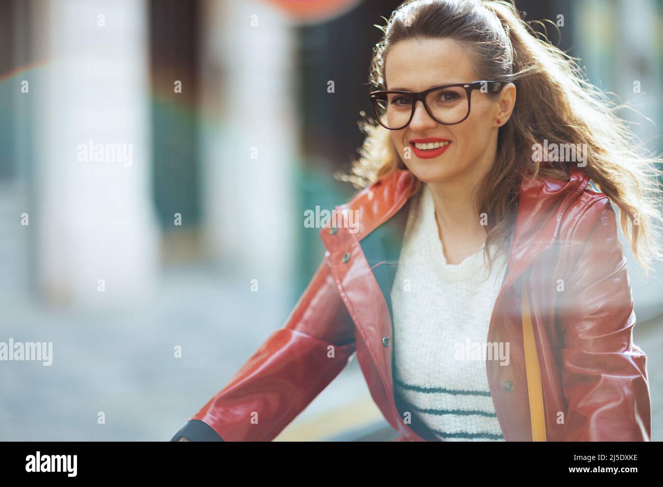 happy elegant woman in red rain coat outdoors on the city street riding ...