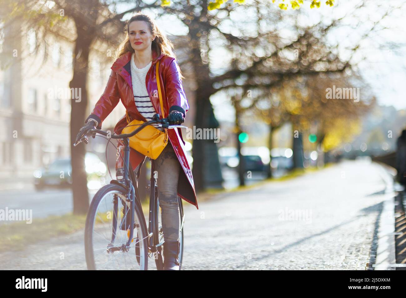 stylish female in red rain coat outside on the city street riding ...
