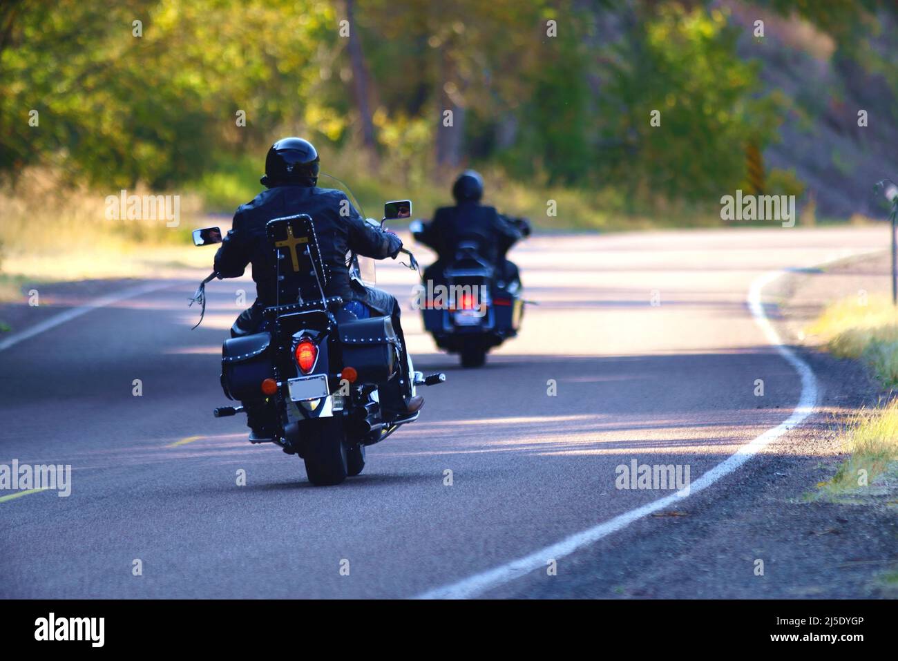 Motorcyclists on a sunny day outing.on a road that curves beside hills with trees. Stock Photo