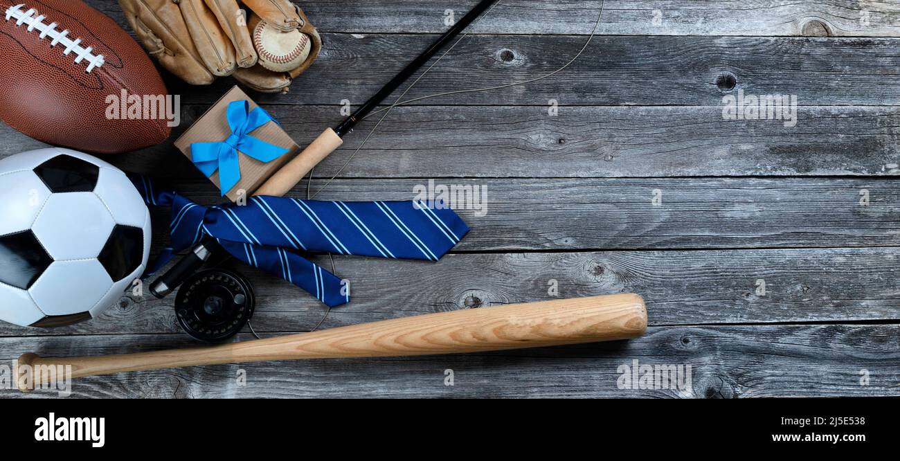 Blue tie, soccer, fishing gear, baseball, bat, football and a gift box on a vintage wood table for Fathers Day concept Stock Photo