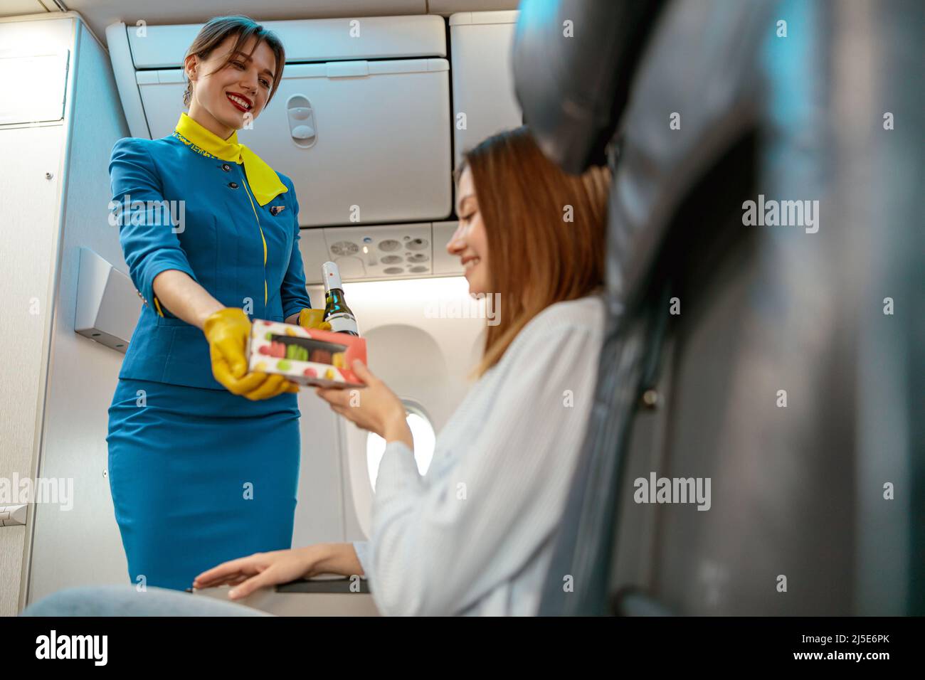 Joyful stewardess giving cookies to woman in airplane Stock Photo