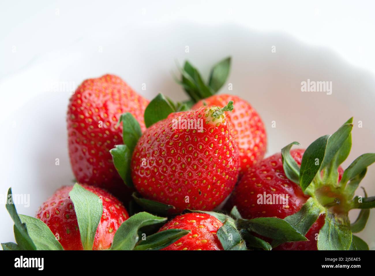 Close-up of strawberry fruit. Some bright red berries on a white dish. Strawberries seeds, between which one is already beginning to germinate. Stock Photo