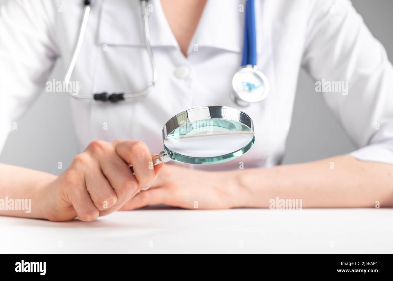 Doctor sitting at table with magnifier. Medical checkup, thorough physical and mental examination. Woman with stethoscope in lab coat holding loupe. High quality photo Stock Photo