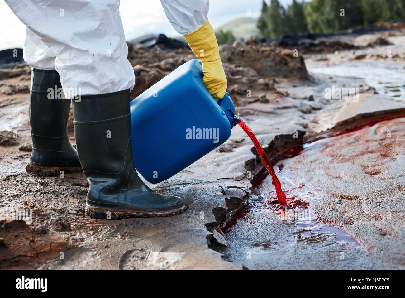 Closeup of unrecognizable ecologist in rubber gloves and boots pouring