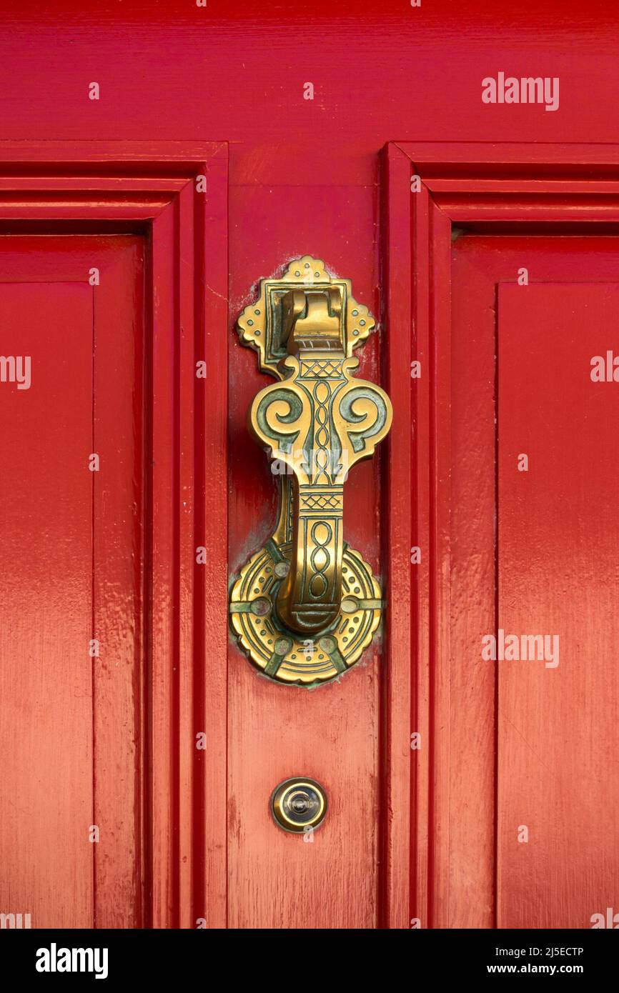 Ornate, decorative brass door knocker on red painted wooden front door with spy glass viewer, UK Stock Photo