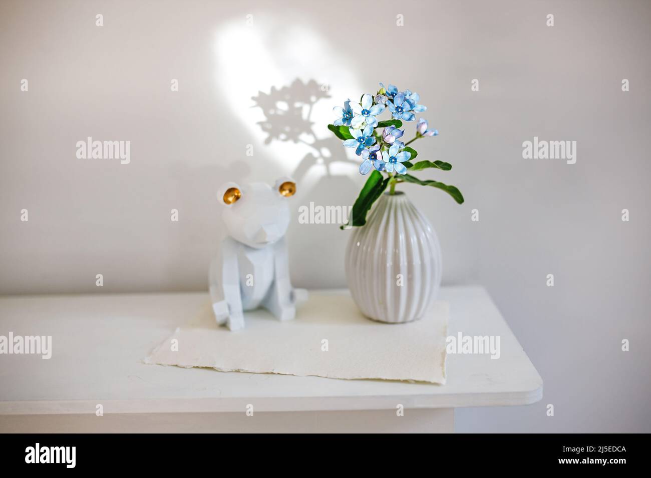Flower hackelia velutina in a white fluted vase in the style of the seventies, a figurine of bear. Scandinavian style. Shadow Stock Photo