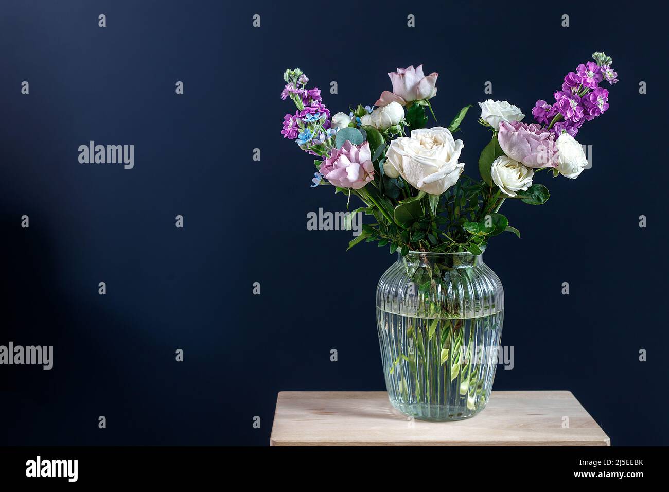 Bouquet of hackelia velutina, purple and white roses, small tea roses, matthiola incana and blue iris in glass vase isolated on black background Stock Photo