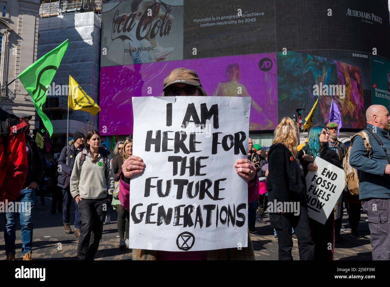 Extinction Rebellion protester in Piccadilly Circus, London, UK, with placard. I am here for the future generations. Carbon neutrality on billboard Stock Photo