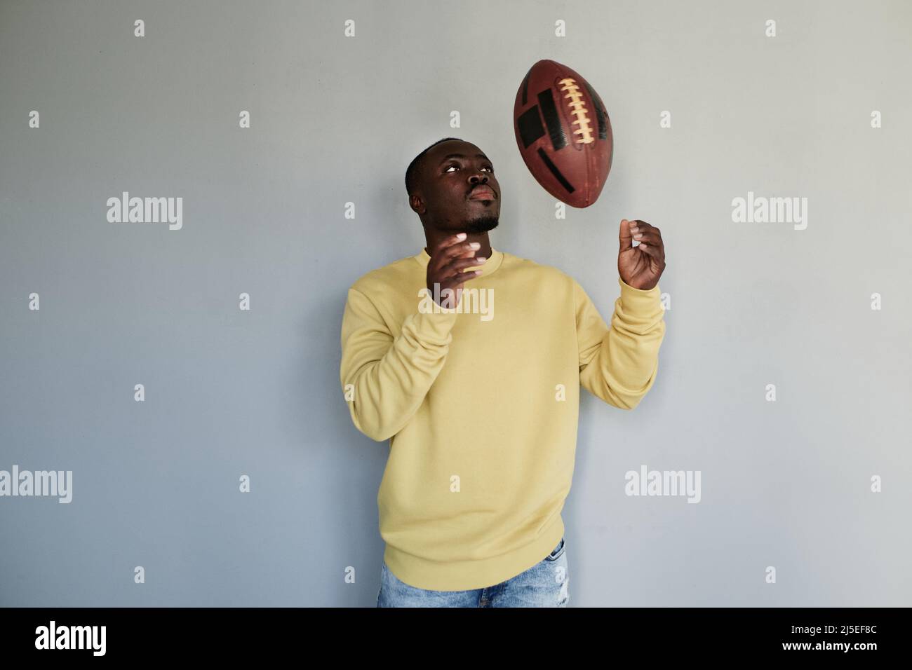 Serious young black rugby player of college team standing against gray