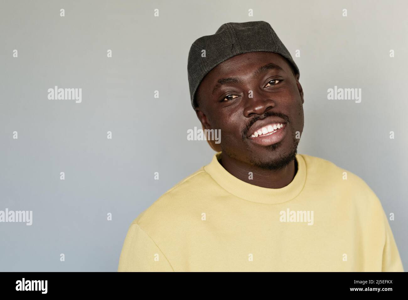 Portrait of happy young black guy in cap and yellow sweatshirt standing against isolated background Stock Photo