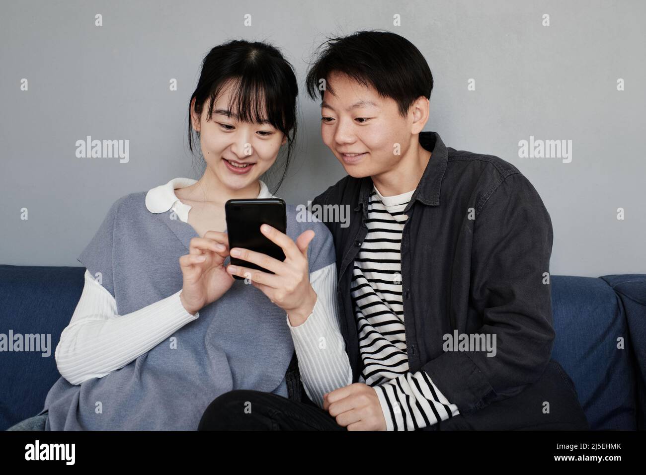 Smiling young Asian couple in casual outfits sitting together and watching  photos on phone Stock Photo - Alamy