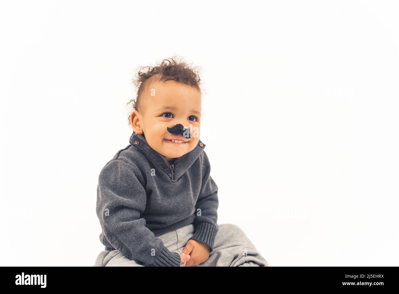 Cute happy small child wearing fake mustache and sitting on the floor, isolated white background. High quality photo Stock Photo