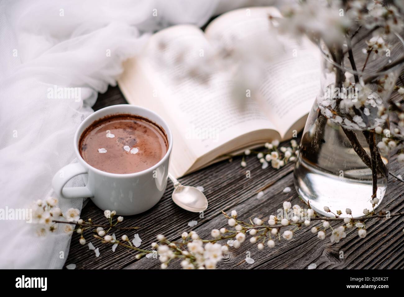 Cup of hot chocolate cacao, old book and spring cherry flowers on wooden background. Reading concept Stock Photo