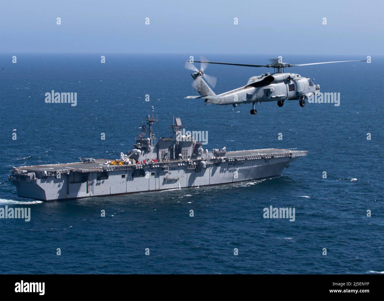 Pacific Ocean, United States. 16 April, 2022. A U.S. Navy MH-60R Sea Hawk helicopter, assigned to Helicopter Maritime Strike Squadron 35, flies past the Wasp-class amphibious assault ship USS Tripoli during routine operations with the 3rd Fleet, April 16, 2021 in the Pacific Ocean.  Credit: MC3 Christopher Sypert/Planetpix/Alamy Live News Stock Photo