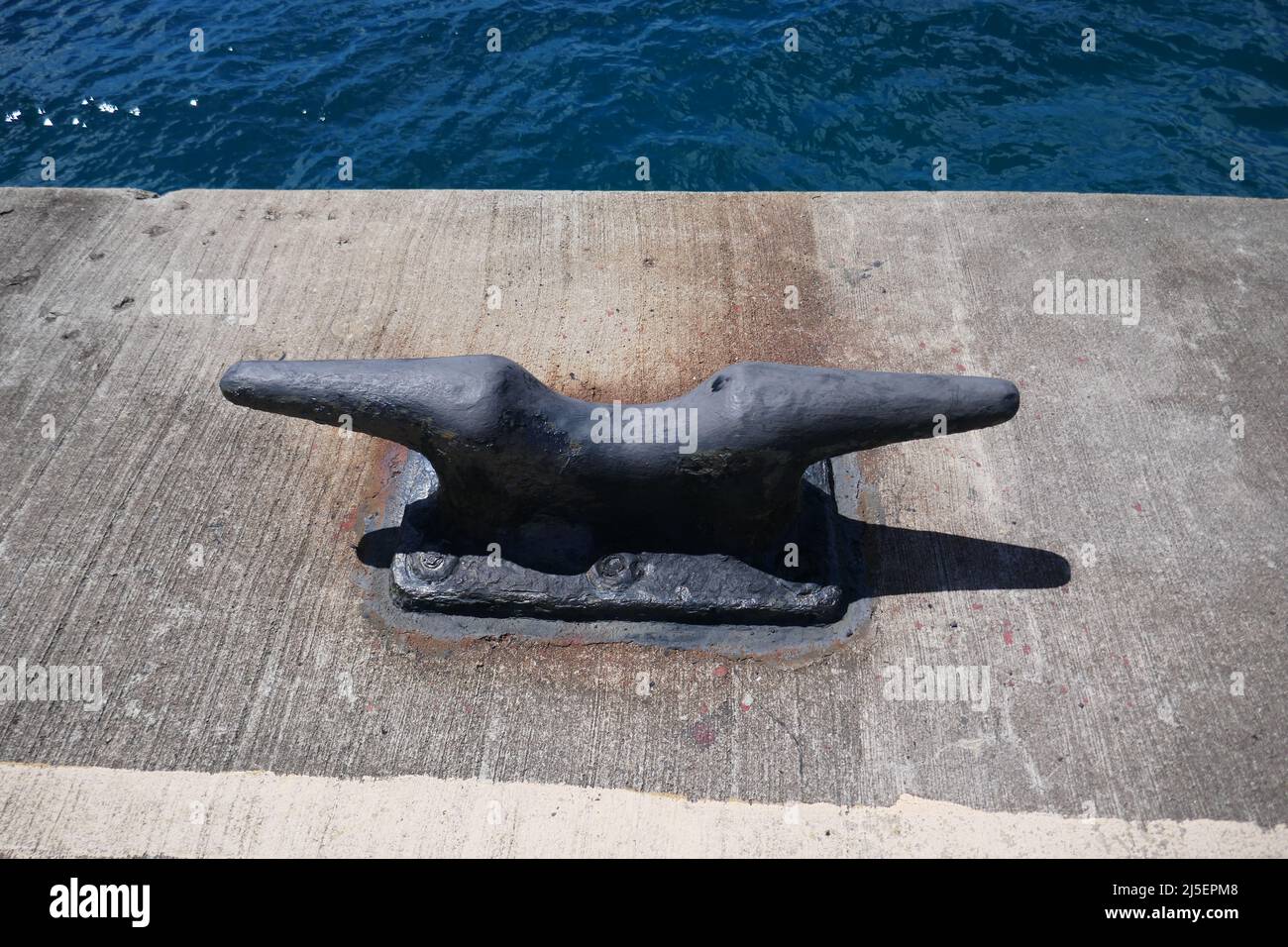 Mooring cleat attached to concrete ship dock with ocean water over side Stock Photo