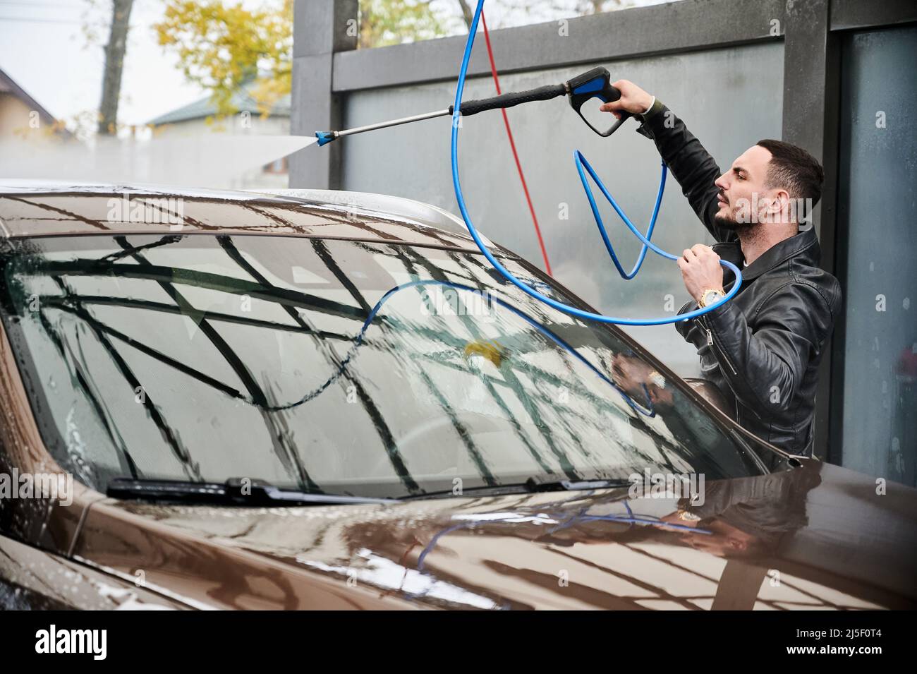 Young man washing car on carwash station outdoor. Handsome driver