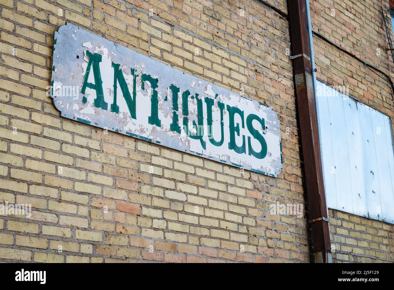 A well weathered sign reading 'antiques' is affixed to a brick wall to advertise a business. Stock Photo