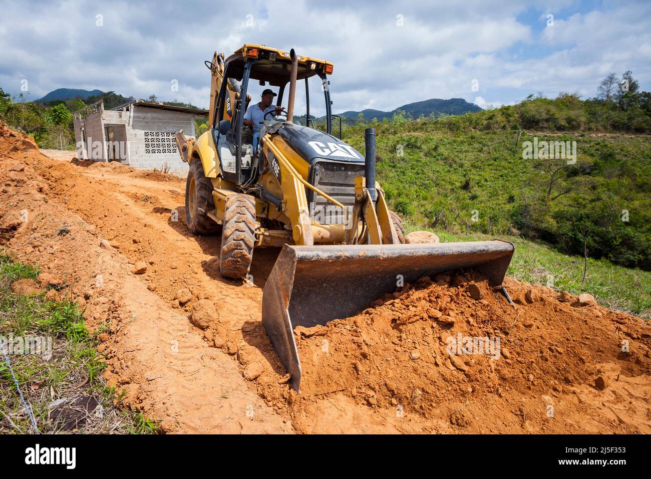 A tractor excavator operator is using the tractor excavator to shovel red earth in a construction site in the Cocle province, Republic of Panama. Stock Photo