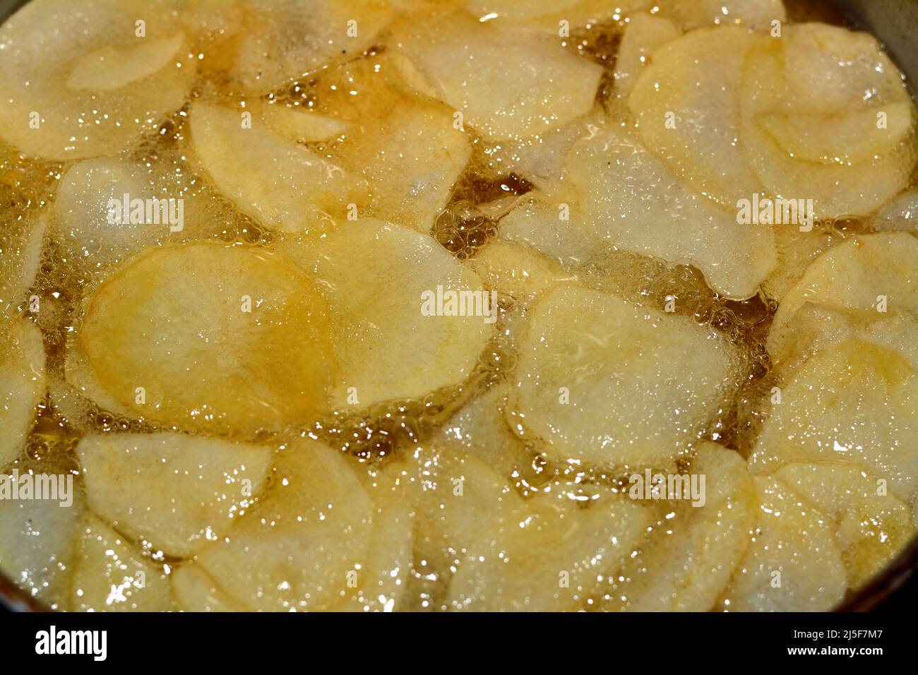 A close up of fried chips potatoes frying in boiling hot oil in a deep