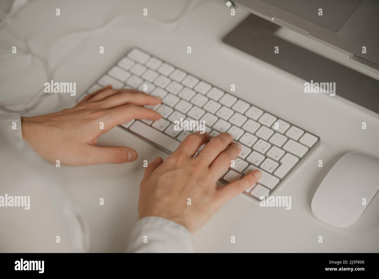 Close-up photo of woman’s hands typing on a wireless white aluminum keyboard Stock Photo