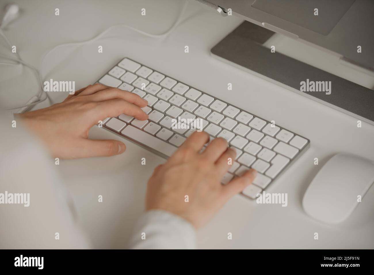 Close-up photo of woman’s hands typing on a wireless white aluminum keyboard. Stock Photo