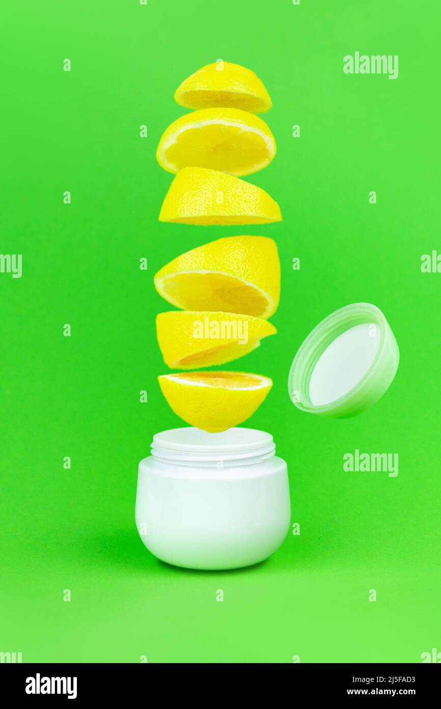 Bottle for cream with flying cover andd fresh lemons on green background. Supplement Bottle Jar Packaging Mockup Stock Photo
