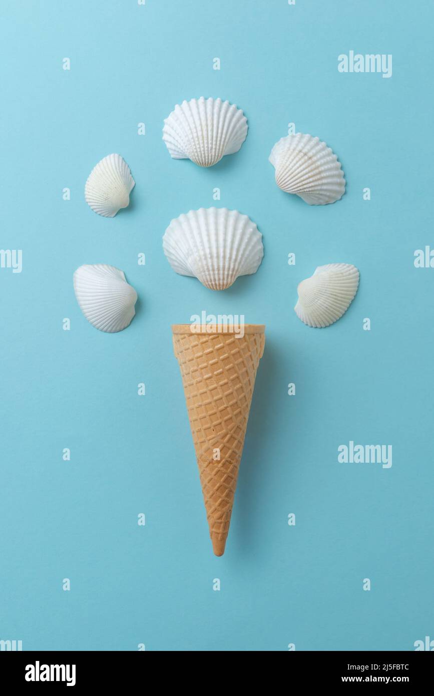Shellfish ice cream concept on blue surface. Ice cream cone with white shells. Stock Photo