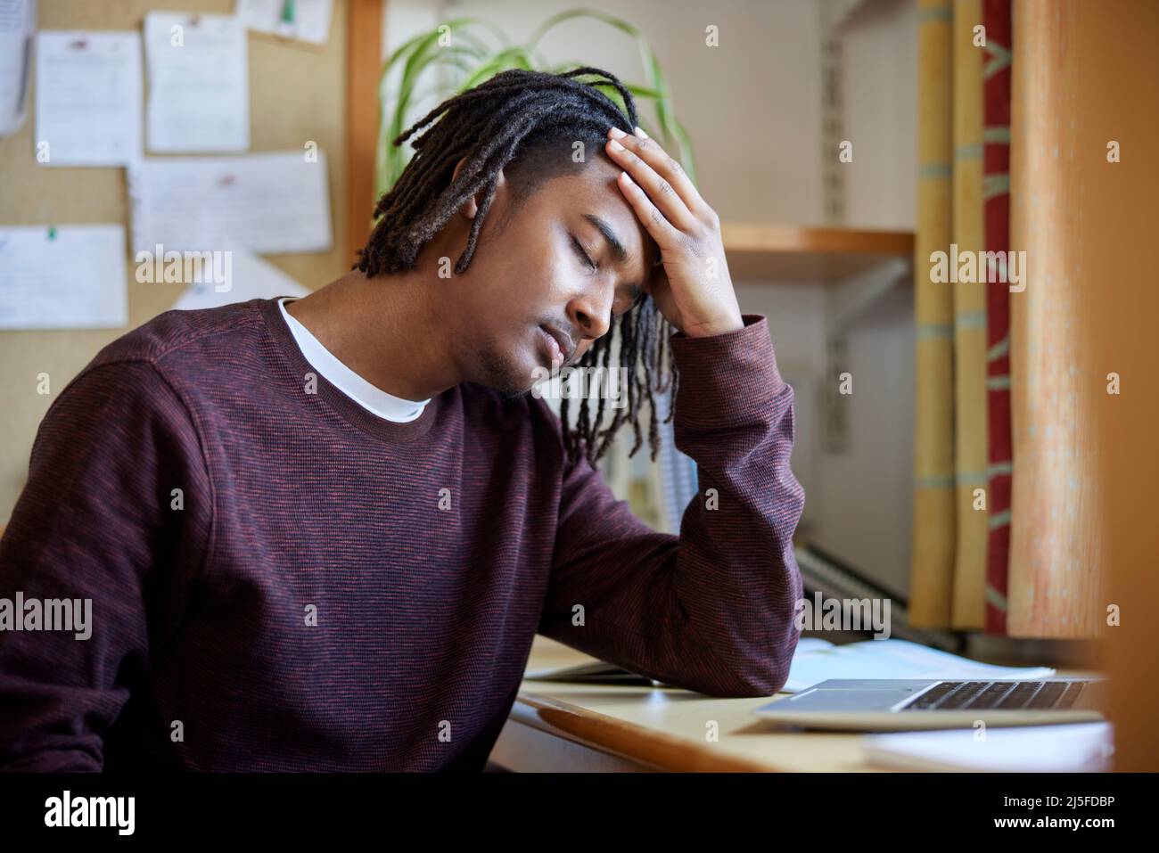 Stressed Male University Or College Student With Poor Mental Health Studying With Laptop At Desk In Room Stock Photo