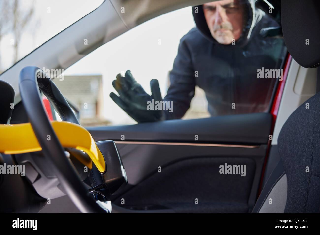 Male Thief Looking Through Window At Manual Steering Wheel Lock In Car Stock Photo