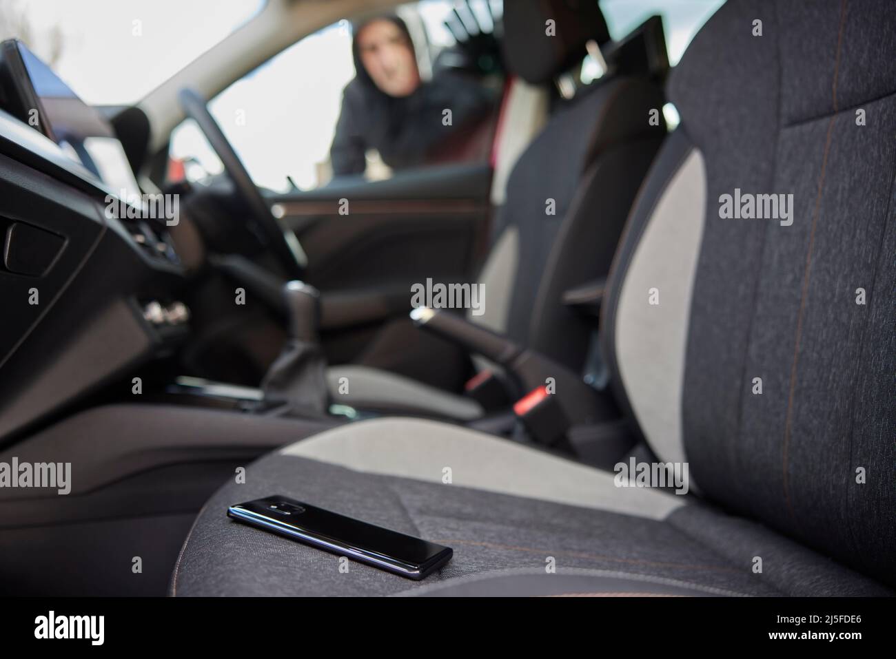 Male Thief Looking Through Car Window At Mobile Phone Left On Seat Stock Photo