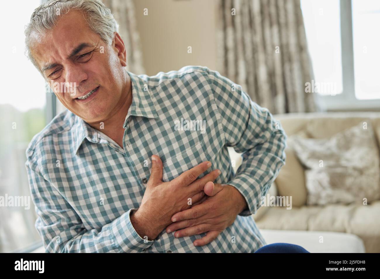 Mature Man Clutching Chest And Suffering Heart Attack At Home Stock Photo