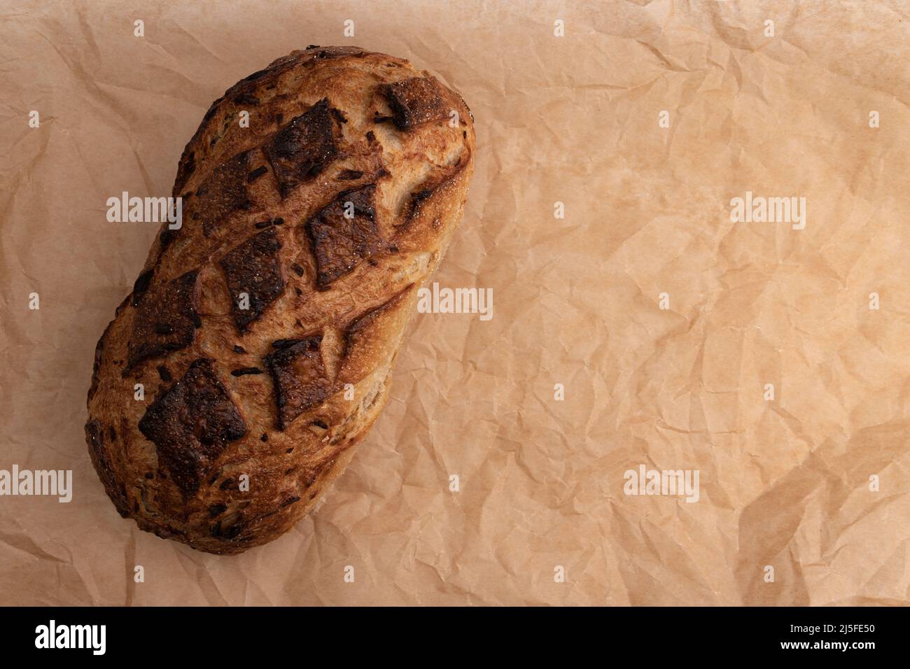 top view of fresh homemade bread with golden crispy crust on parchment for baking, organic loaf with onion close-up and space for text Stock Photo