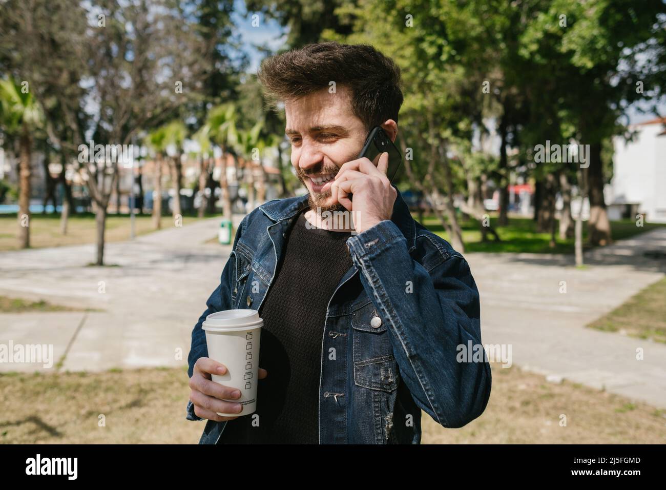 Smiling young man, handsome man holding coffee cup making voice call