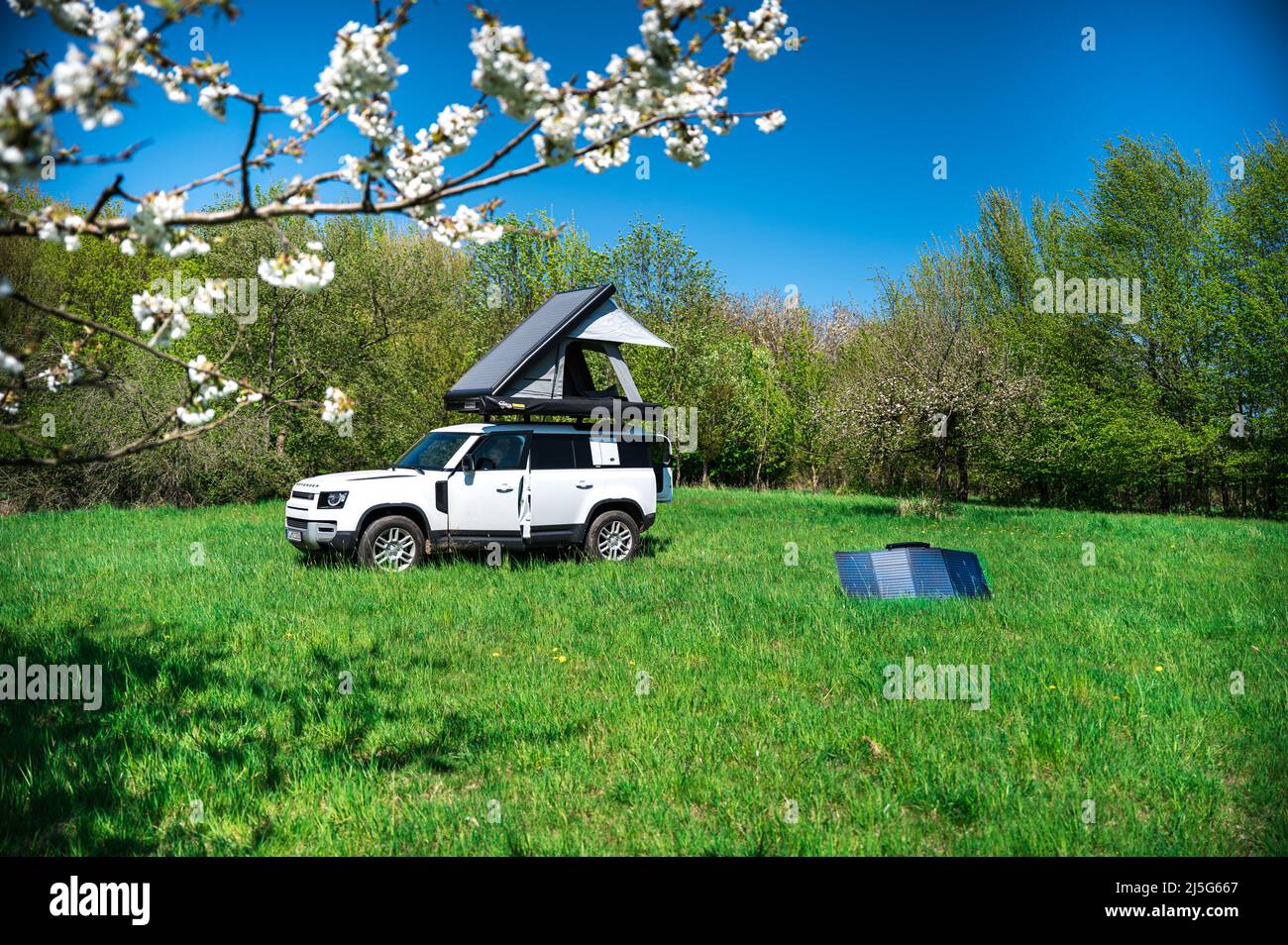 4x4 Offroad vehicle camping with roof tent in a meadwow with solar panel for energy generation in foreground Stock Photo