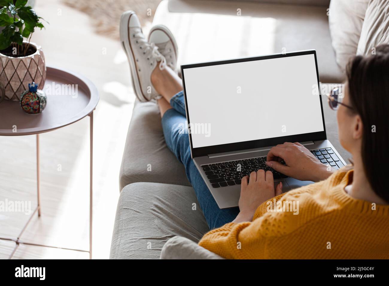 Young woman using laptop screen blank, mockup lying on sofa at home ...