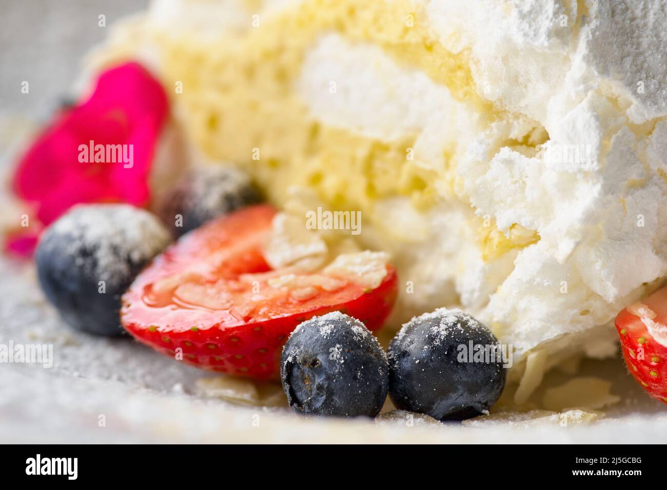 meringue roll with strawberries, blueberries, raspberries and cranberries. Dessert decorated with fresh berries on table. Stock Photo