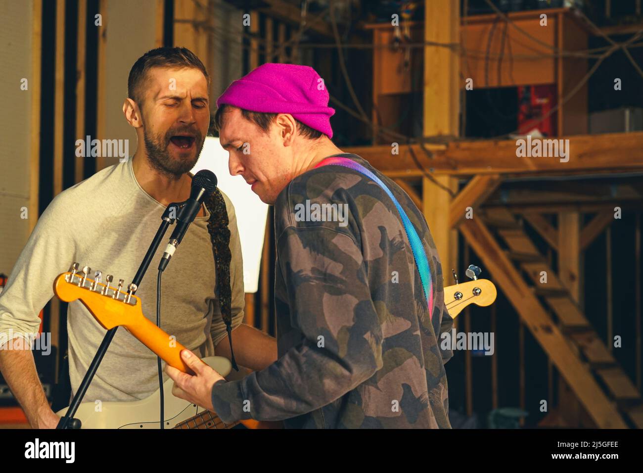 Two guys play electric guitars and sing into the microphone. Bass guitarist and vocals guitarist Stock Photo