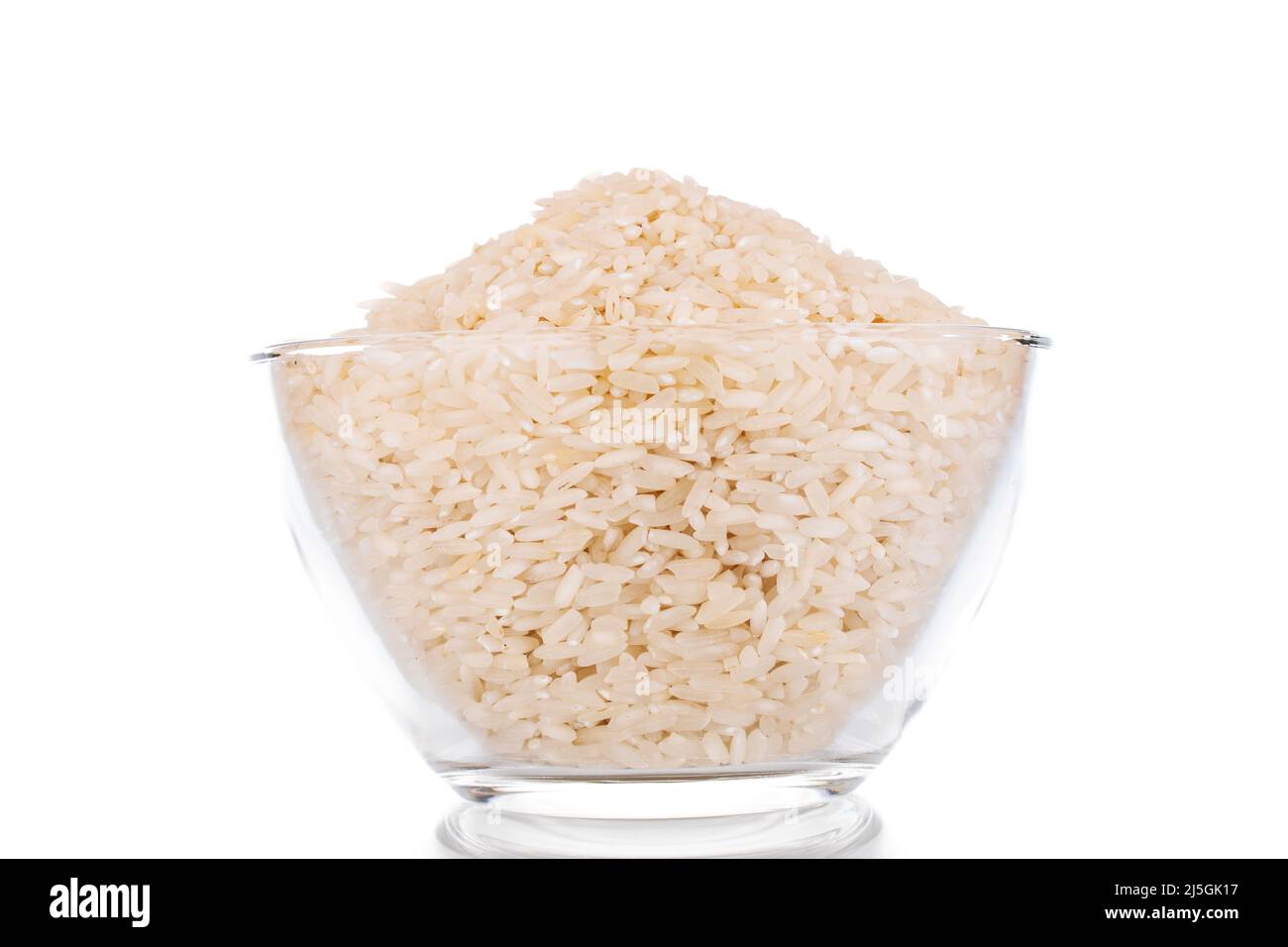 Uncooked organic rice in a glass bowl, macro, isolated on a white background. Stock Photo