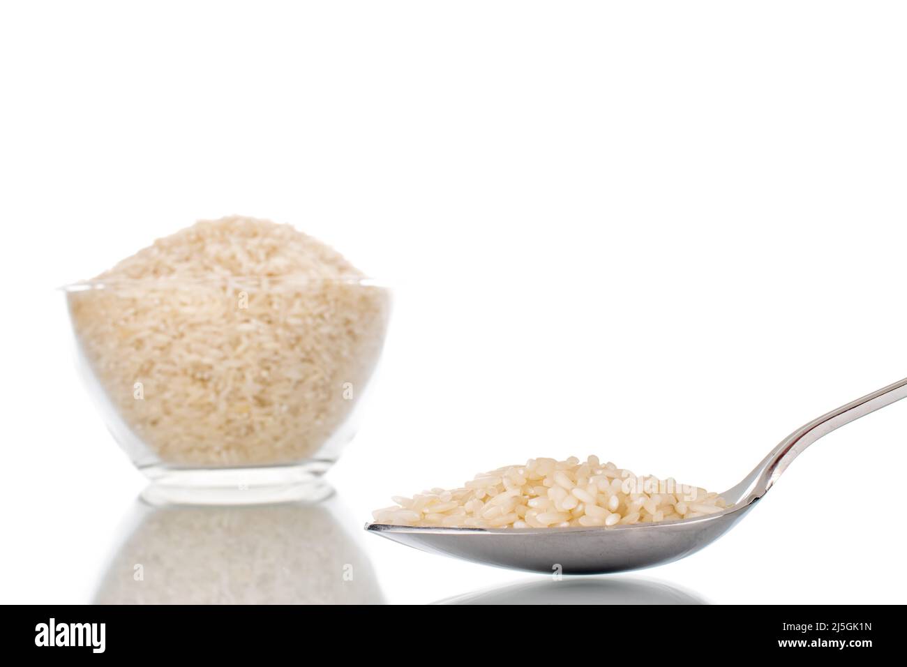 Uncooked organic rice with metal spoon and glassware, macro, isolated on white background. Stock Photo