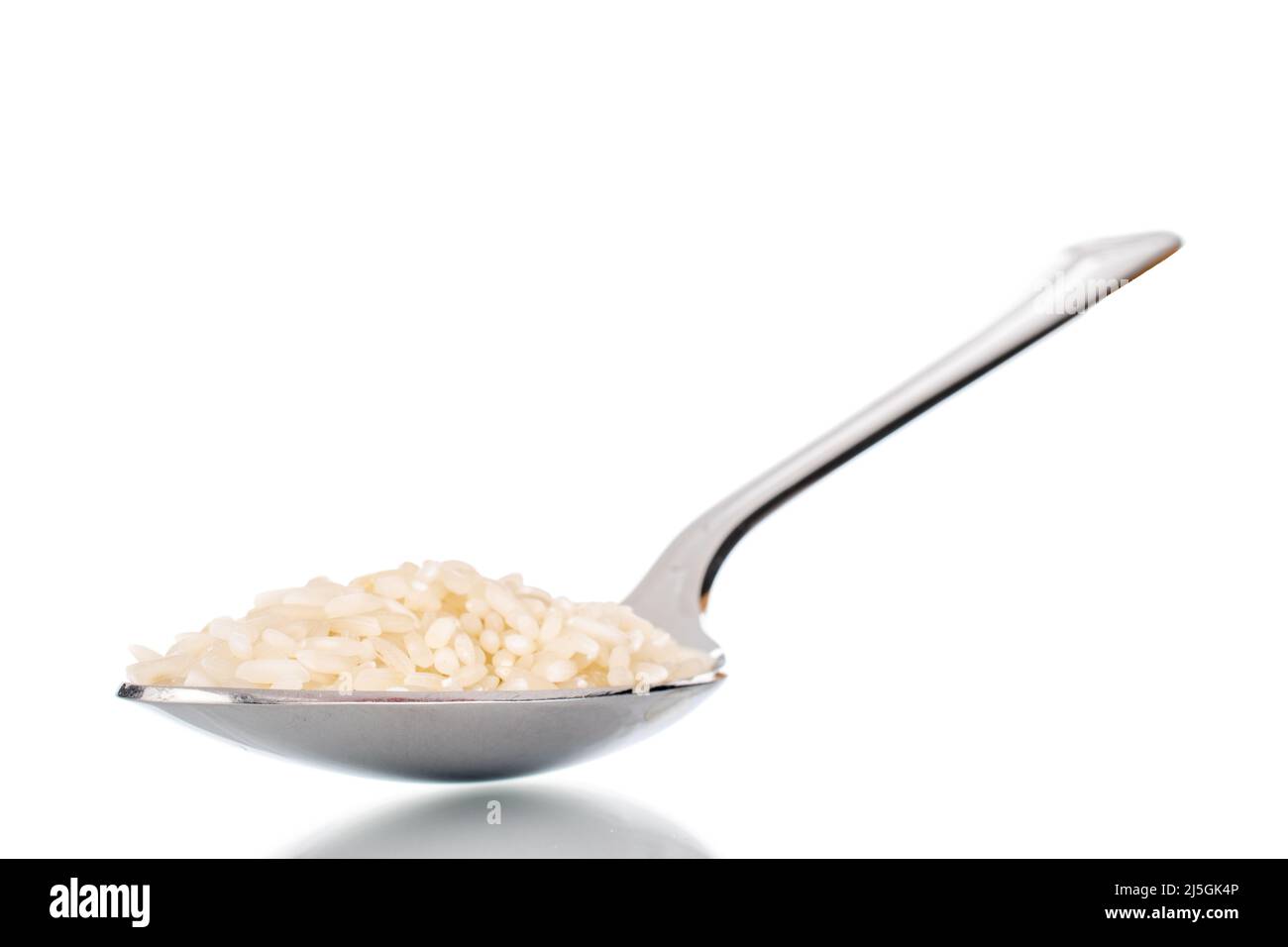Uncooked organic rice with a metal spoon, close-up, isolated on a white background. Stock Photo